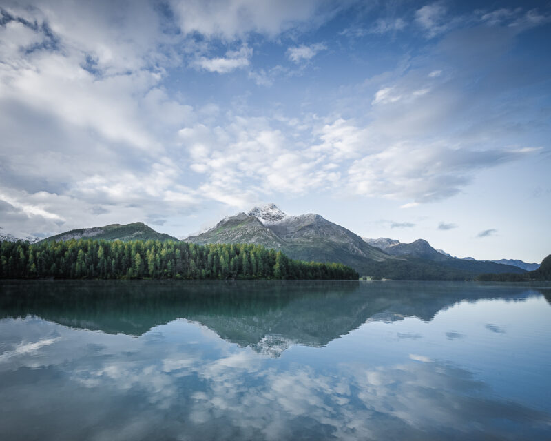 lken spiegeln sich im windstillen Silsersee im Engadin vor der Berglandschaft der Schweizer Alpen.